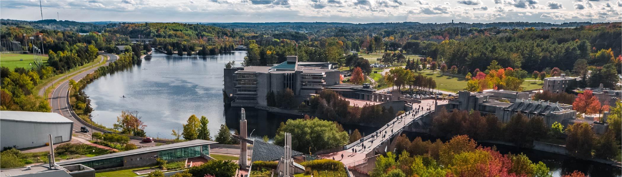 Aerial photograph of Trent University. Faryon bridge in foreground, Otonabee river in left third, and Bata Library Centre. 