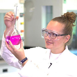 Woman in lab coat holding up beaker of liquid