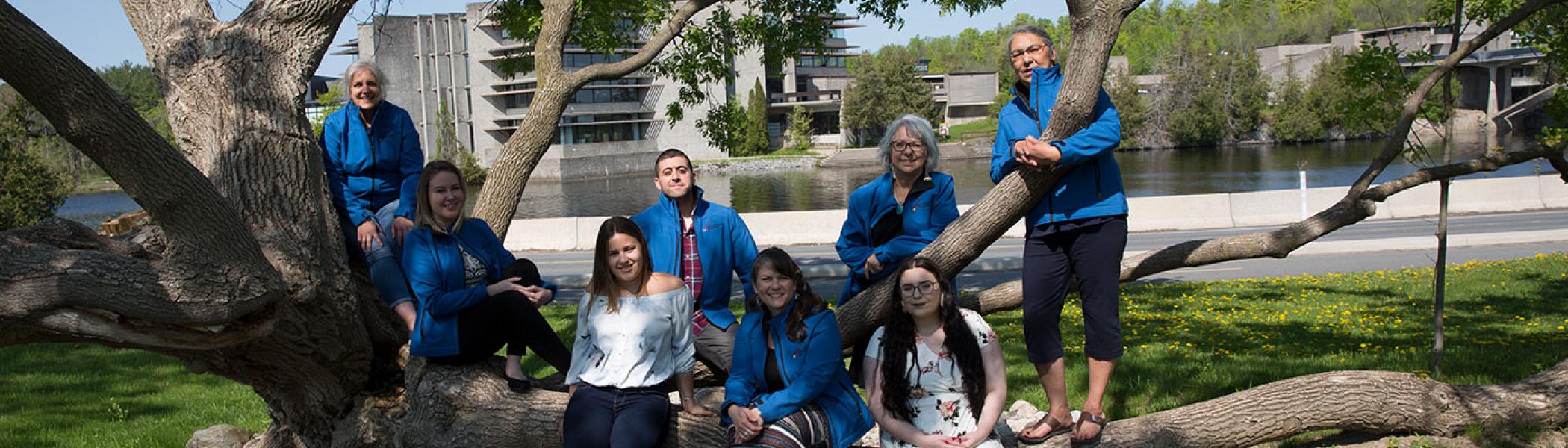 FPHL Department team sitting on a tree outside on a summer day.