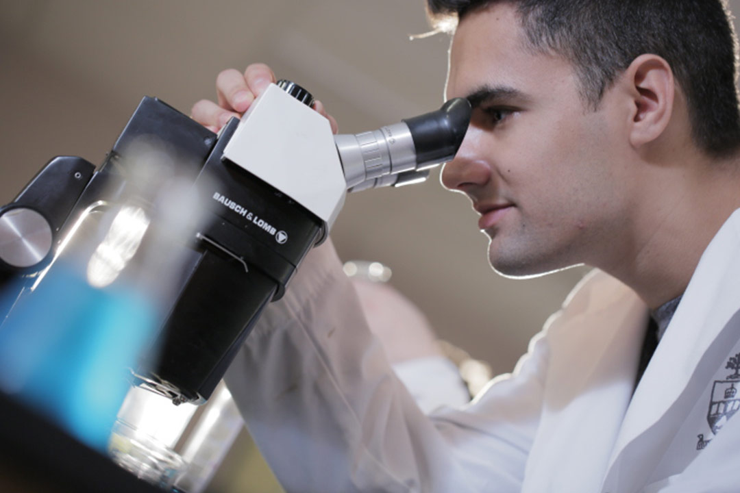 Man in lab coat looking into microscope