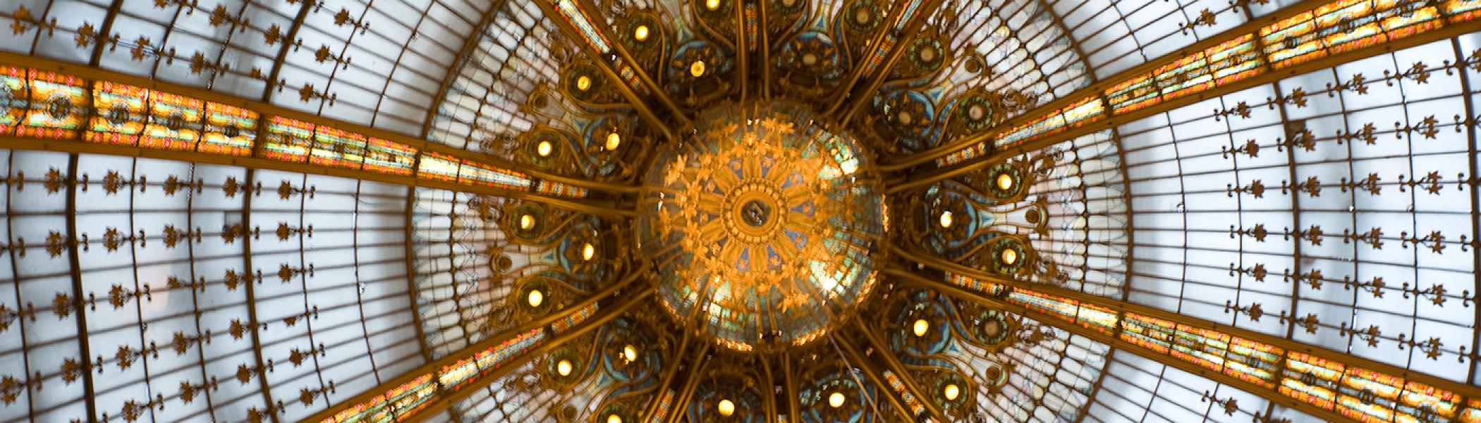 Looking up and intricate stained glass and gold ceiling with an ornate light in the centre. 