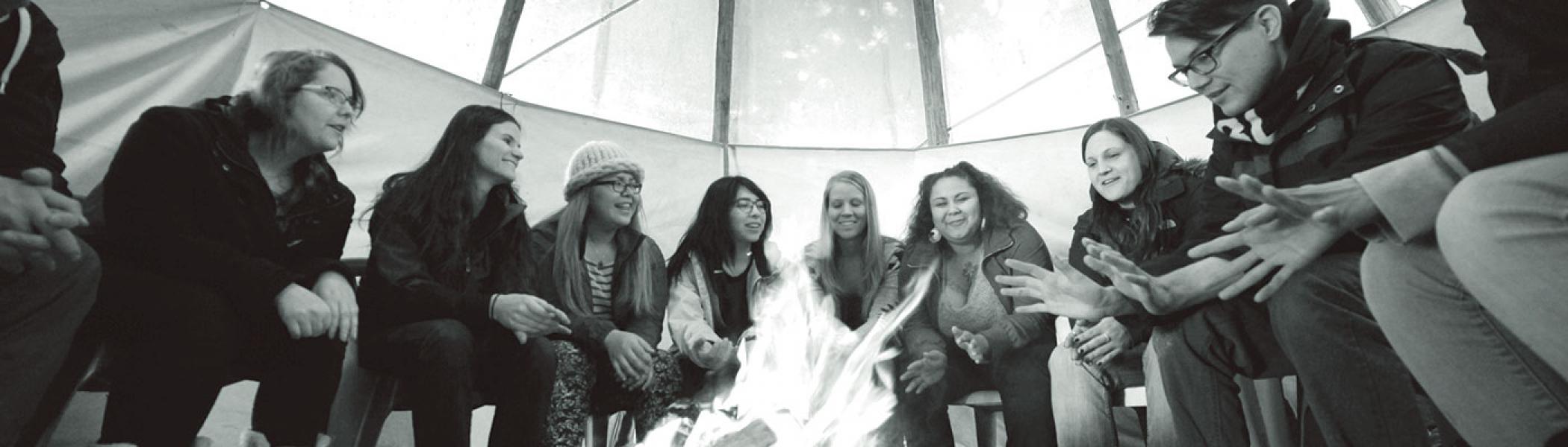 A group of students gathered in a tipi around a fire for class in the late fall