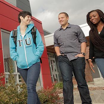 Three students walking past the entrance to Trent University Durham campus