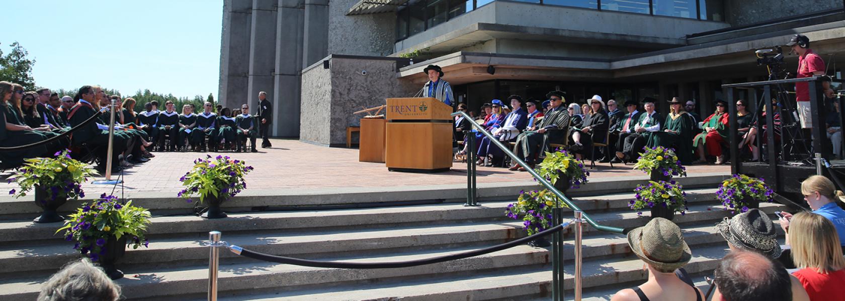 Dr. Leo Groarke standing talking into a podium microphone during convocation outisde of the Bata library