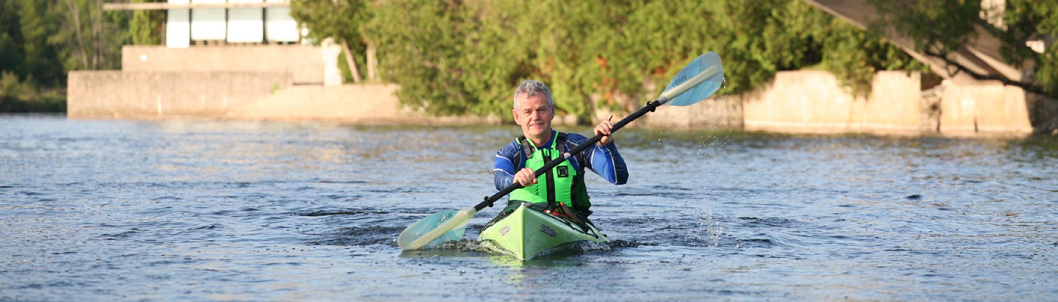 Dr. Leo Groarke kayaking on the Otonabee river in front of the Bata Library
