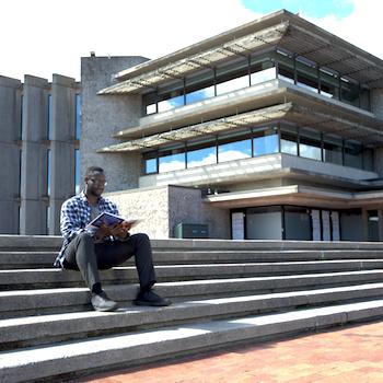A guy sitting on the steps of Bata Library reading a book