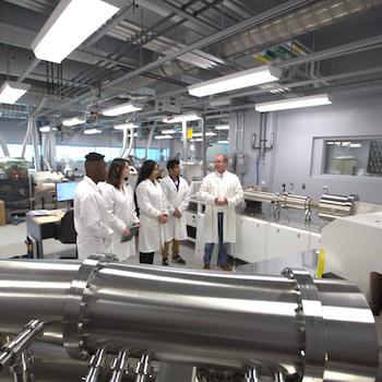 A group of students in lab coats standing with a professor in a lab